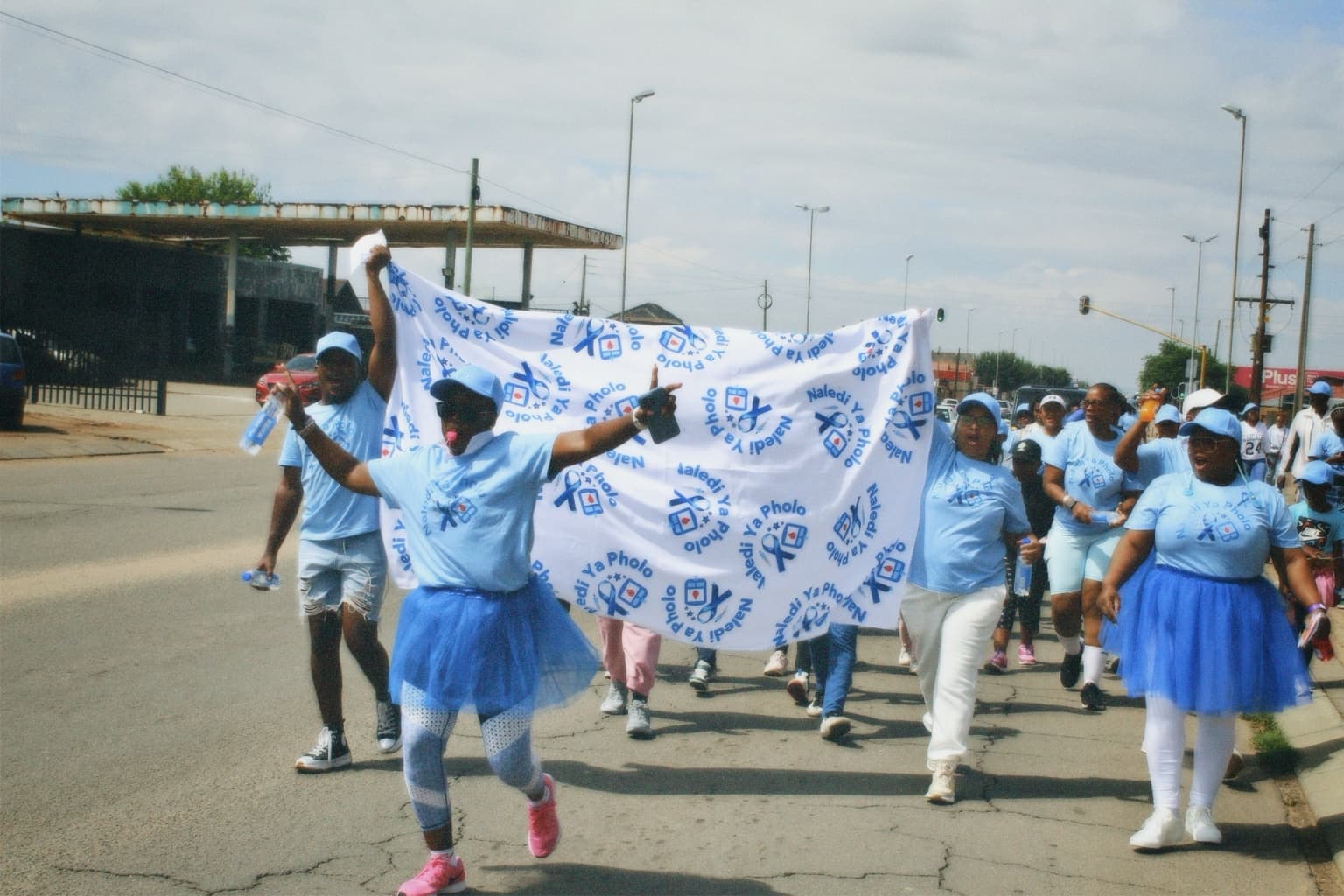 Naledi Ya Pholo participants in blue and white clothing carrying a branded awareness walk banner